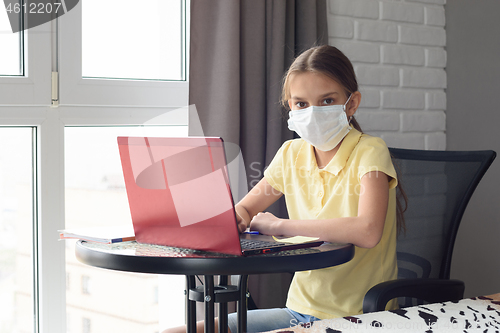 Image of A sick girl sits at a table and is engaged in learning online, looked into the frame