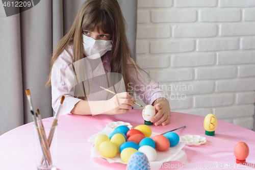 Image of Sad sick quarantined girl paints Easter eggs