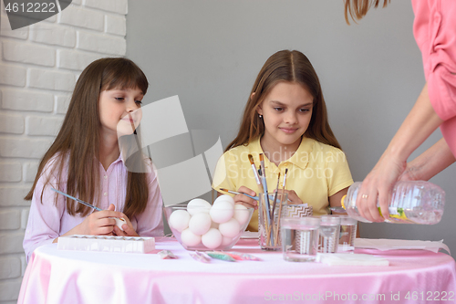 Image of Mom pours vinegar into glasses with food coloring, children at the table prepare to paint eggs