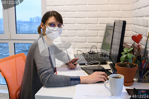 Image of An ill girl in a medical mask in self-isolation works remotely, looked into the frame