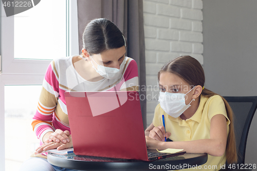 Image of The tutor at home in a medical mask explains to the girl the course of solving homework