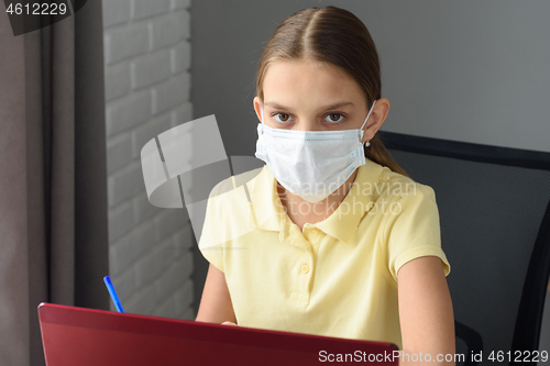 Image of Girl in medical mask studying at a laptop at home