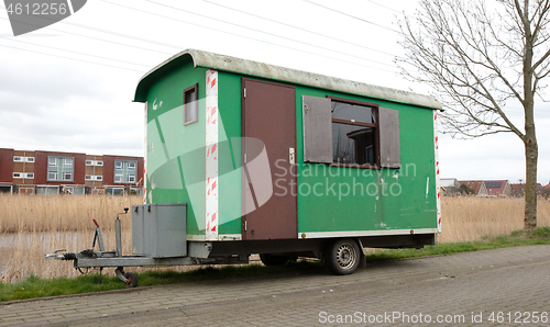 Image of Old green wooden trailer on wheels stands at the side of the roa