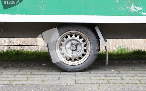 Image of Wheel of an old green wooden trailer on wheels stands at the sid