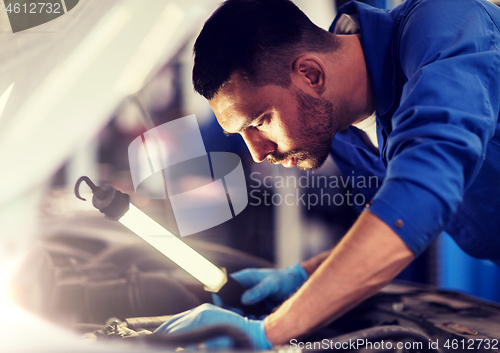 Image of mechanic man with lamp repairing car at workshop