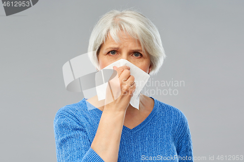 Image of sick senior woman blowing nose to paper napkin