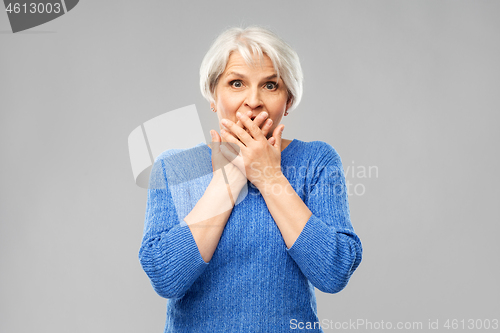 Image of confused senior woman covering her mouth by hands