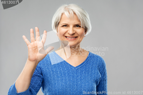 Image of smiling senior woman showing palm or five fingers