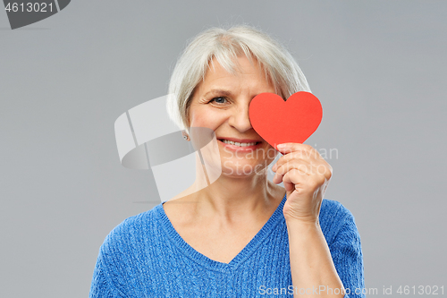 Image of smiling senior woman covering eye with red heart