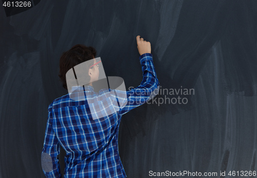 Image of Teen Boy with chalk in hand writing on empty black board in scho