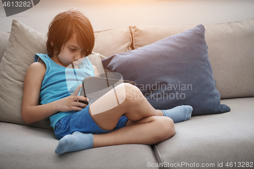 Image of Little Arabian boy sitting on sofa and playing game on digital t