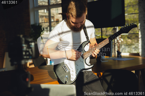 Image of Caucasian musician playing guitar during online concert at home isolated and quarantined, impressive improvising