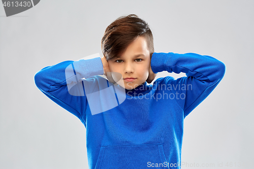 Image of stressed boy in blue sweater closing ears by hands