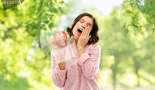 Image of sleepy woman in pajama with alarm clock yawning