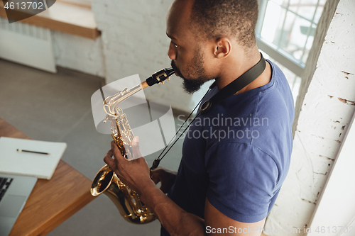 Image of African-american musician playing saxophone during online concert at home isolated and quarantined, impressive improvising