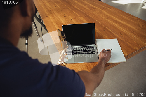 Image of African-american musician playing saxophone during online concert at home isolated and quarantined. Blank laptop screen with copyspace.