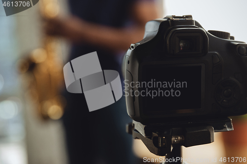 Image of African-american musician playing saxophone during online concert at home isolated and quarantined, focus on camera