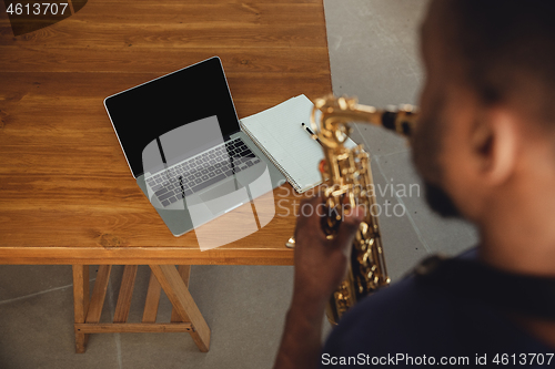 Image of African-american musician playing saxophone during online concert at home isolated and quarantined. Blank laptop screen with copyspace.