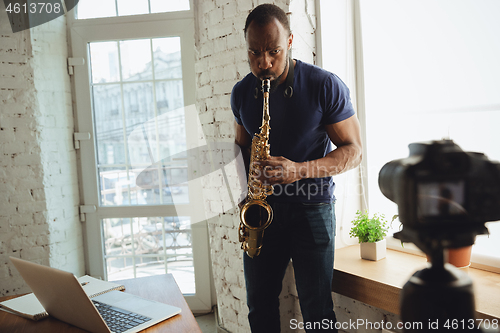 Image of African-american musician playing saxophone during online concert at home isolated and quarantined, improvising on camera