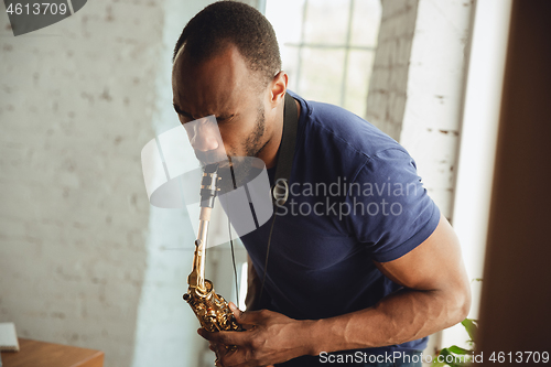 Image of African-american musician playing saxophone during online concert at home isolated and quarantined, attented, focused