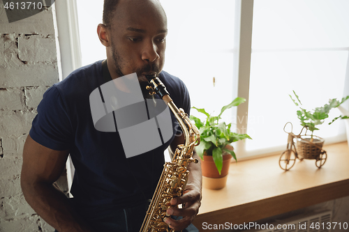 Image of African-american musician playing saxophone during online concert at home isolated and quarantined, impressive improvising