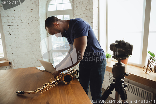 Image of African-american musician playing saxophone during online concert at home isolated and quarantined, attented, focused