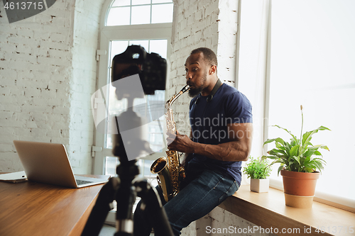 Image of African-american musician playing saxophone during online concert at home isolated and quarantined