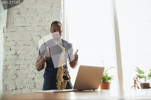 Image of African-american musician playing saxophone during online concert at home isolated and quarantined