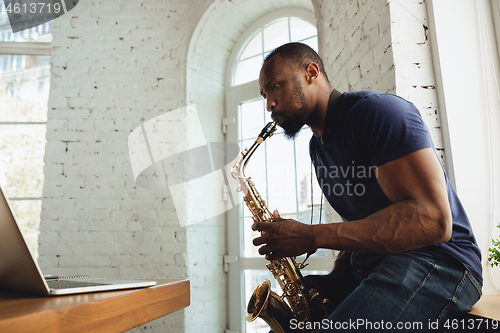 Image of African-american musician playing saxophone during online concert at home isolated and quarantined, impressive improvising