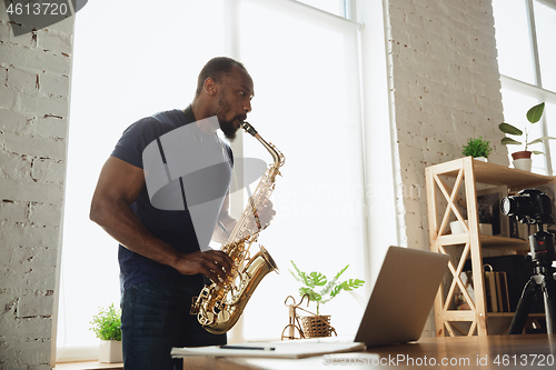 Image of African-american musician playing saxophone during online concert at home isolated and quarantined