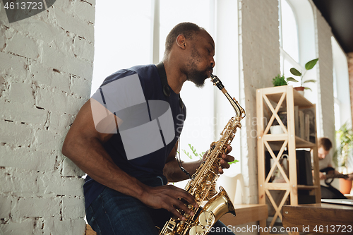 Image of African-american musician playing saxophone during online concert at home isolated and quarantined, impressive improvising