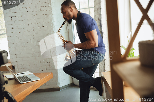 Image of African-american musician playing saxophone during online concert at home isolated and quarantined, impressive improvising