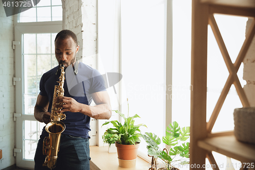 Image of African-american musician playing saxophone during online concert at home isolated and quarantined, attented, focused