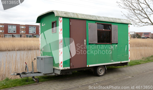 Image of Old green wooden trailer on wheels stands at the side of the roa