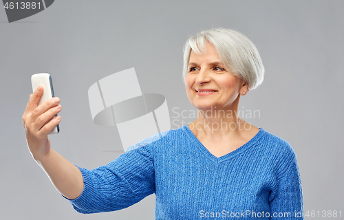 Image of smiling senior woman taking selfie by smartphone