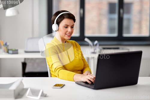 Image of creative woman in headphones with laptop at office