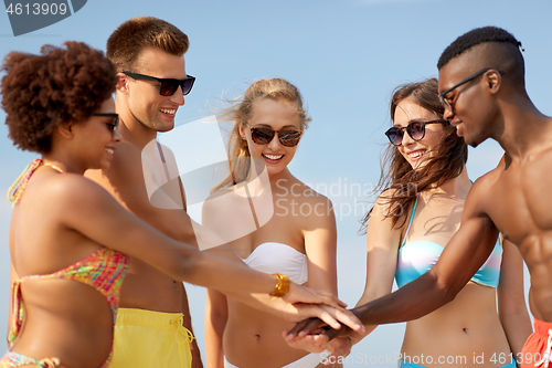 Image of happy friends stacking hands on summer beach