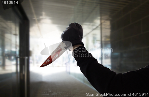 Image of hand in glove with blood on knife over dark tunnel