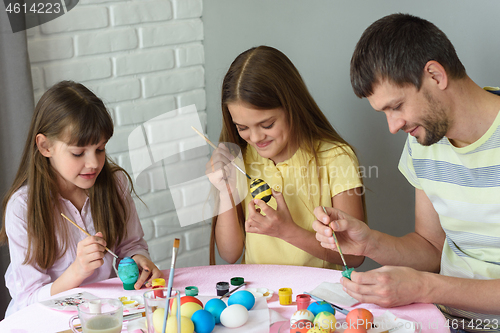 Image of Dad with two daughters paint eggs for Easter holiday
