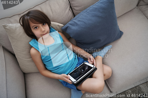 Image of Little Arabian boy sitting on sofa and playing game on digital t