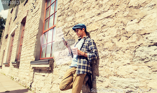 Image of man with smartphone drinking coffee on city street