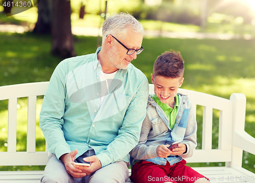 Image of old man and boy with smartphones at summer park