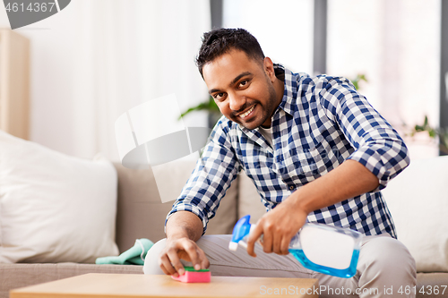 Image of indian man cleaning table with detergent at home