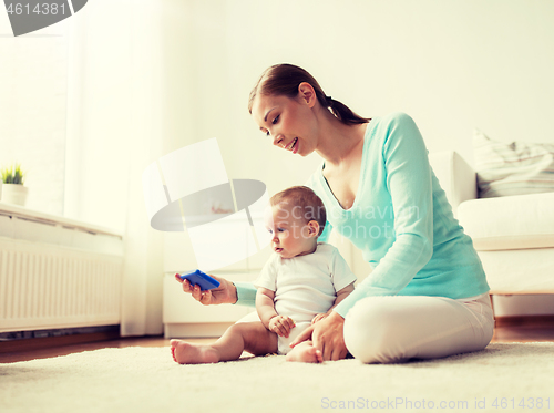 Image of happy mother showing smartphone to baby at home