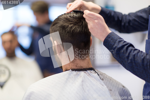 Image of male hairdresser cutting hair at barbershop