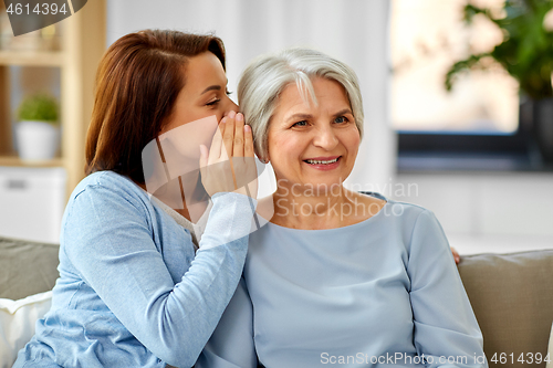 Image of adult daughter whispering to senior mother at home