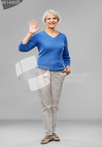 Image of senior woman waving hand over grey background