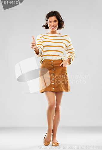 Image of woman in pullover, skirt and shoes shows thumbs up