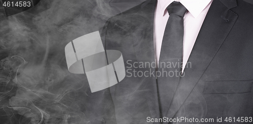 Image of Man in a black suit, standing in smoke, close-up