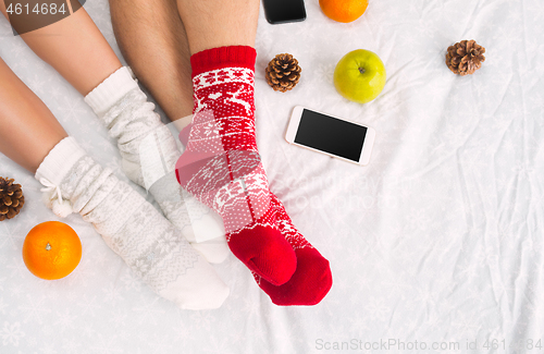 Image of Soft photo of woman and man on the bed with phone and fruits, top view point. Female and male legs in warm woolen socks